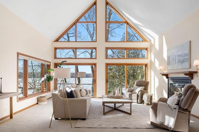 carpeted living room featuring high vaulted ceiling, a glass covered fireplace, a wealth of natural light, and baseboards