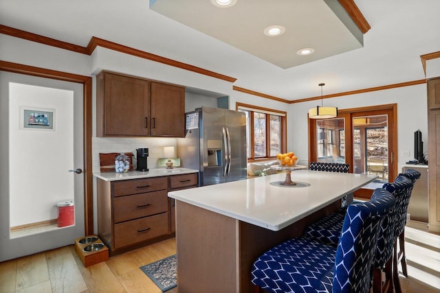 kitchen with a breakfast bar area, light wood-style flooring, light countertops, stainless steel fridge with ice dispenser, and crown molding