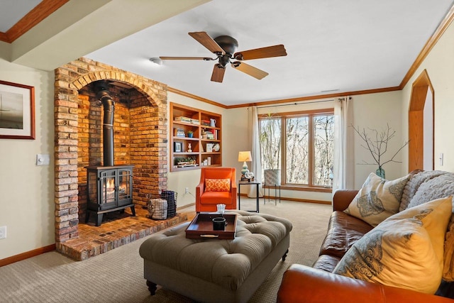 carpeted living room featuring built in shelves, ornamental molding, a wood stove, ceiling fan, and baseboards