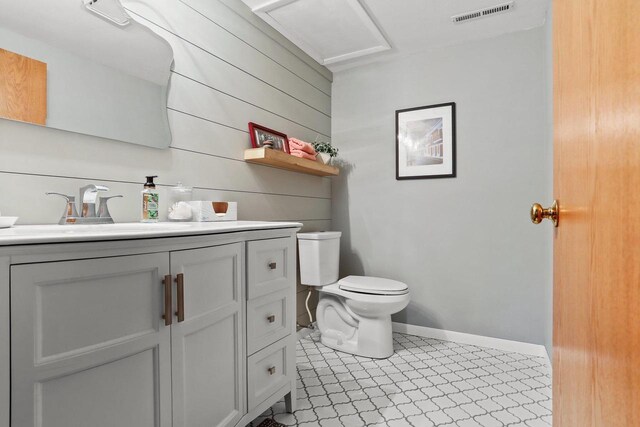 half bath featuring baseboards, visible vents, toilet, vanity, and wood walls