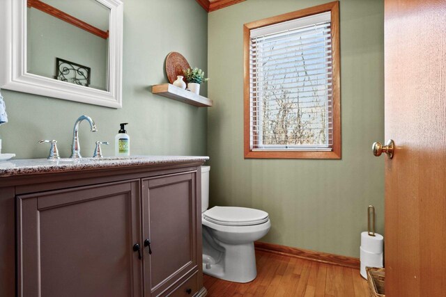 half bathroom featuring toilet, baseboards, wood finished floors, and vanity