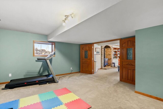 exercise area with a wood stove, light colored carpet, and baseboards