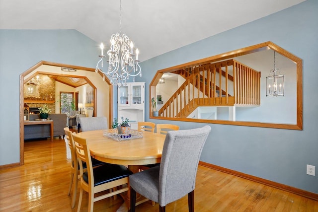 dining space featuring baseboards, lofted ceiling, wood-type flooring, a fireplace, and a notable chandelier