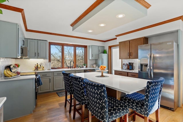 kitchen featuring a kitchen island, ornamental molding, a breakfast bar area, light countertops, and stainless steel refrigerator with ice dispenser