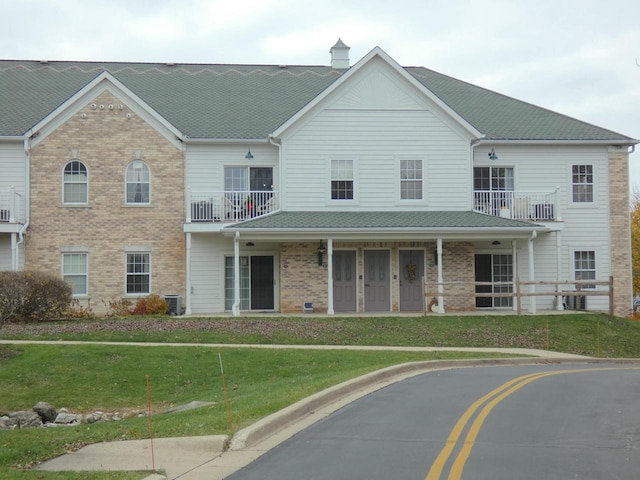 view of front facade featuring a balcony, a front lawn, cooling unit, and brick siding