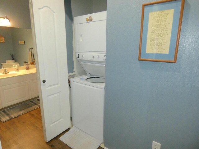 laundry room with a sink, laundry area, wood finished floors, and stacked washer and clothes dryer