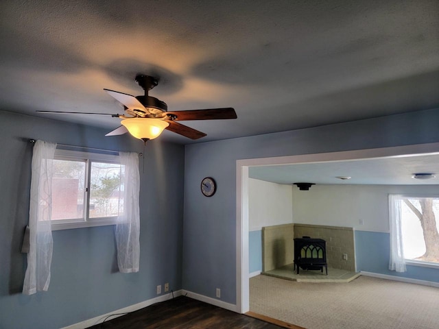 unfurnished living room featuring baseboards, dark wood-type flooring, ceiling fan, and a wood stove