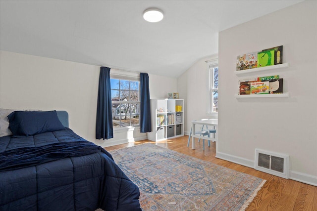 bedroom with vaulted ceiling, wood finished floors, visible vents, and baseboards