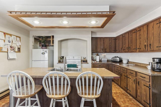 kitchen featuring a baseboard radiator, white appliances, a sink, a kitchen breakfast bar, and an island with sink