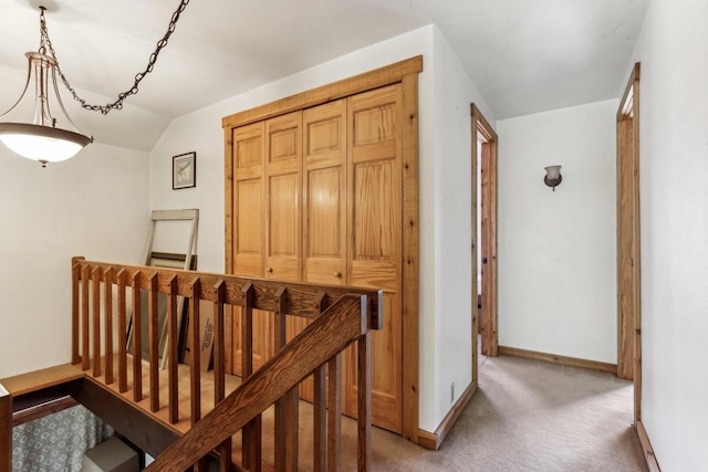 hall featuring an upstairs landing, lofted ceiling, light colored carpet, and baseboards