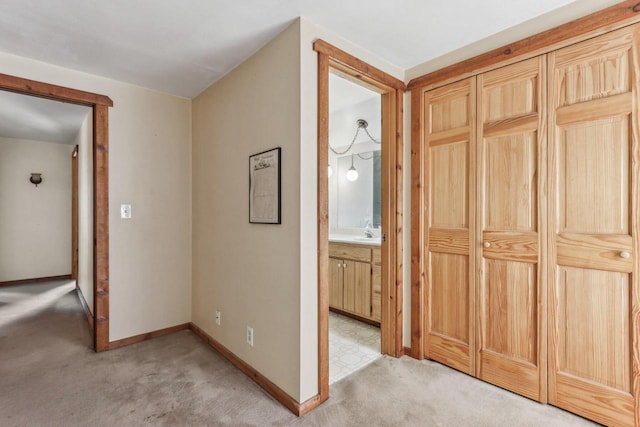 hall featuring baseboards, a sink, and light colored carpet