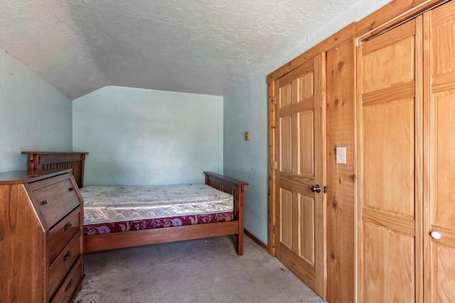 bedroom featuring vaulted ceiling, a textured ceiling, and light colored carpet