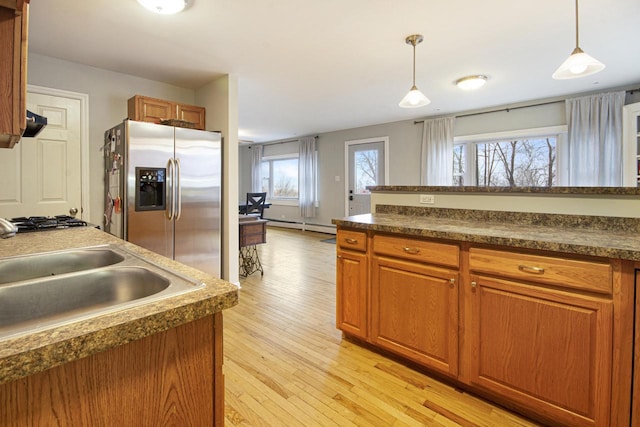 kitchen with light wood-type flooring, appliances with stainless steel finishes, brown cabinetry, and dark countertops