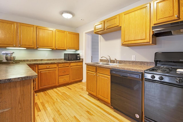 kitchen with dark countertops, light wood-style floors, a sink, under cabinet range hood, and black appliances