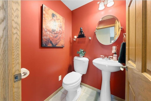 half bathroom with baseboards, a sink, toilet, and tile patterned floors