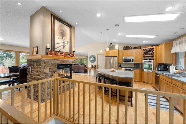 kitchen with a fireplace, stainless steel appliances, lofted ceiling, light wood-style floors, and a sink