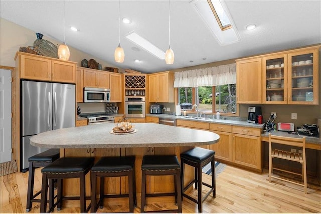 kitchen featuring vaulted ceiling with skylight, appliances with stainless steel finishes, a kitchen breakfast bar, and a sink