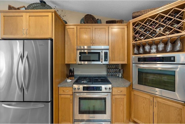 kitchen with lofted ceiling, appliances with stainless steel finishes, and a textured ceiling