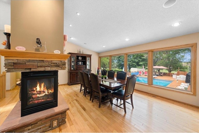 dining space featuring light wood-type flooring, a fireplace, vaulted ceiling, and a textured ceiling