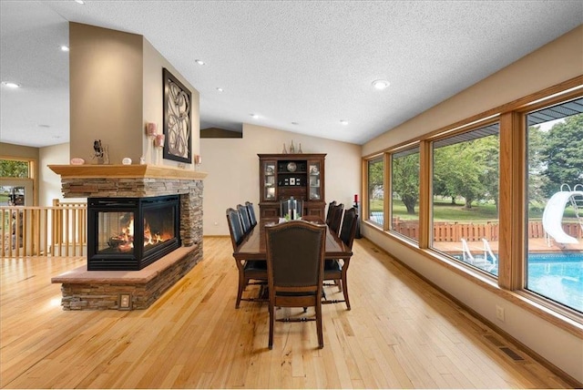 dining space with a textured ceiling, a stone fireplace, visible vents, vaulted ceiling, and wood-type flooring