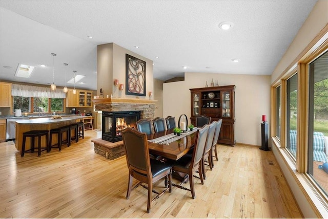 dining space featuring a textured ceiling, a stone fireplace, light wood-style flooring, baseboards, and vaulted ceiling