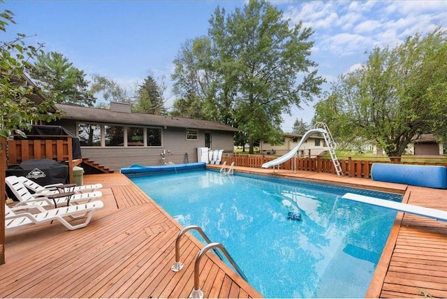 view of pool with a diving board, a water slide, a wooden deck, and a covered pool