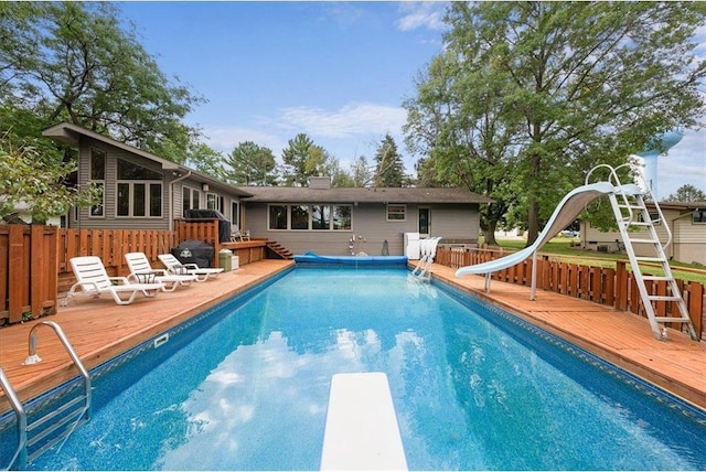 view of pool with a fenced in pool, a water slide, a wooden deck, and a diving board