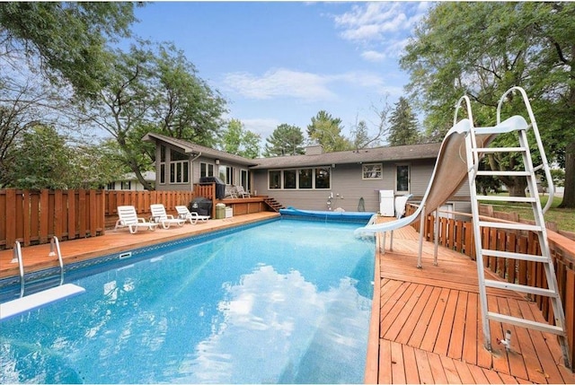 view of pool with a fenced in pool, fence, a water slide, a wooden deck, and a diving board