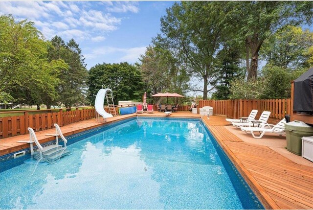 view of swimming pool with a deck, a water slide, fence, and a fenced in pool