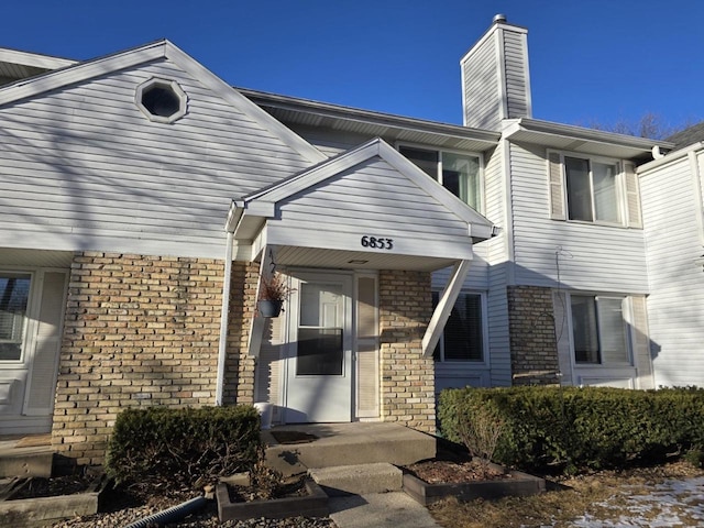 view of exterior entry with brick siding and a chimney