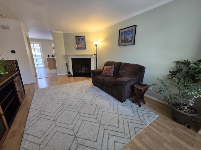 living room featuring a fireplace with flush hearth, baseboards, crown molding, and light wood finished floors