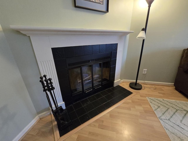 interior details featuring a tile fireplace, baseboards, and wood finished floors