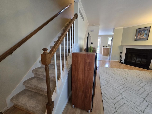 stairway featuring a fireplace with flush hearth, baseboards, crown molding, and wood finished floors