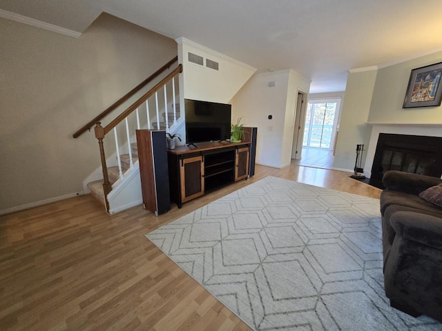 living room with a fireplace with flush hearth, stairs, light wood-style flooring, and crown molding