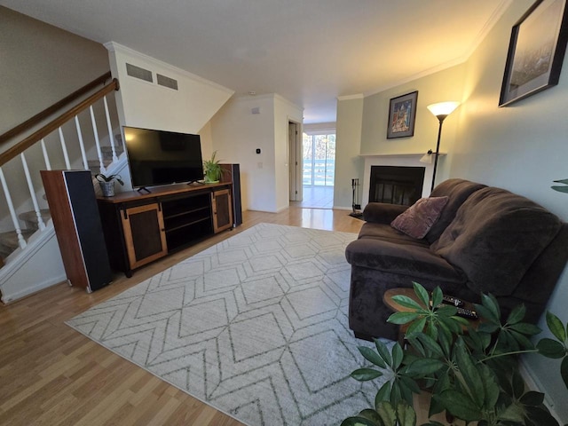 living area featuring visible vents, stairway, wood finished floors, crown molding, and a fireplace