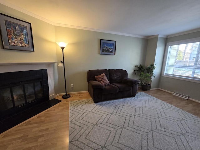 living area with visible vents, a tiled fireplace, ornamental molding, wood finished floors, and baseboards