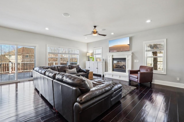 living area featuring ceiling fan, recessed lighting, dark wood finished floors, baseboards, and a glass covered fireplace