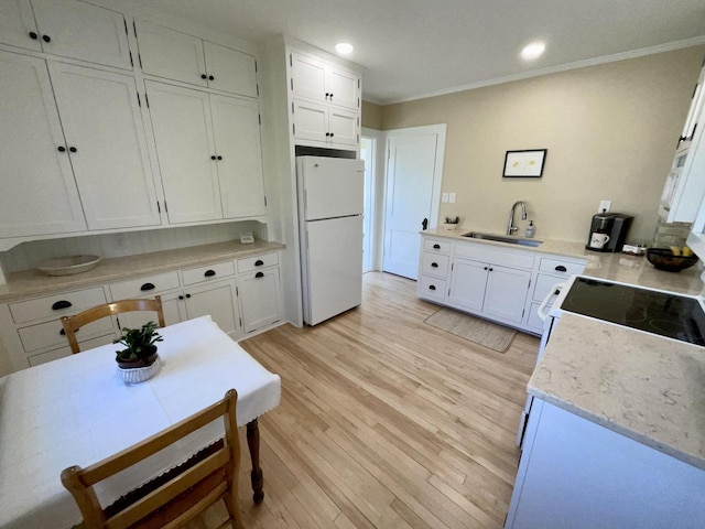 kitchen with a sink, freestanding refrigerator, and white cabinetry