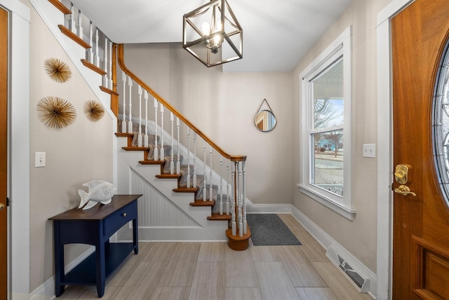 foyer entrance featuring stairway, baseboards, visible vents, and a chandelier