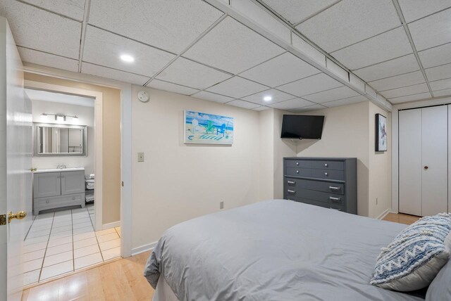 bedroom featuring light wood-type flooring, a closet, baseboards, and a paneled ceiling