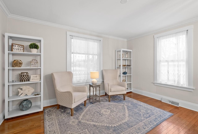 living area with baseboards, crown molding, visible vents, and hardwood / wood-style floors