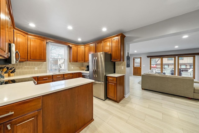 kitchen with light countertops, backsplash, appliances with stainless steel finishes, open floor plan, and a sink