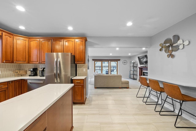 kitchen featuring decorative backsplash, appliances with stainless steel finishes, brown cabinets, light countertops, and a fireplace