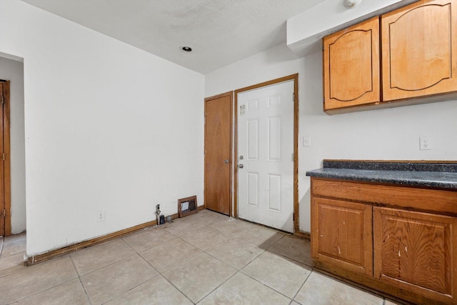 kitchen with dark countertops, light tile patterned floors, baseboards, and brown cabinetry