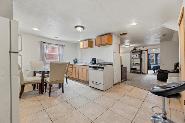 kitchen featuring white appliances, light tile patterned floors, visible vents, light colored carpet, and a textured ceiling