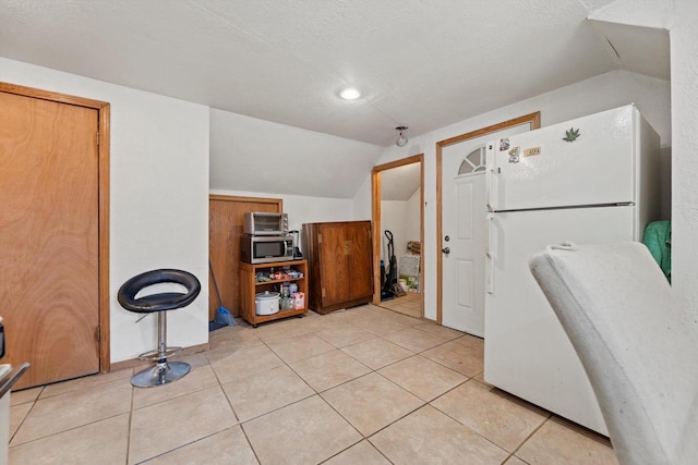 interior space with vaulted ceiling, light tile patterned floors, stainless steel microwave, and freestanding refrigerator