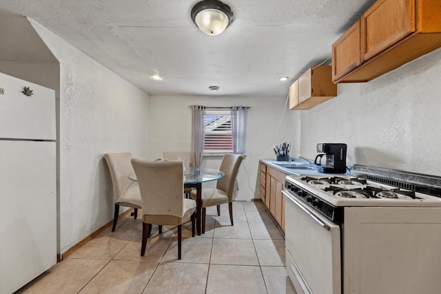 kitchen featuring white appliances, light tile patterned floors, brown cabinets, and a textured wall