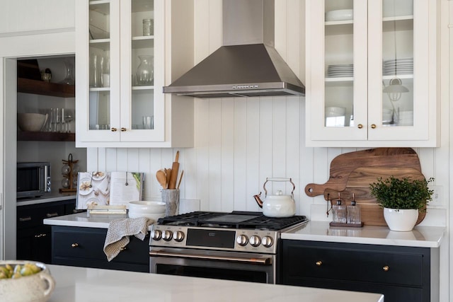 kitchen featuring dark cabinets, gas range, wall chimney exhaust hood, and light countertops