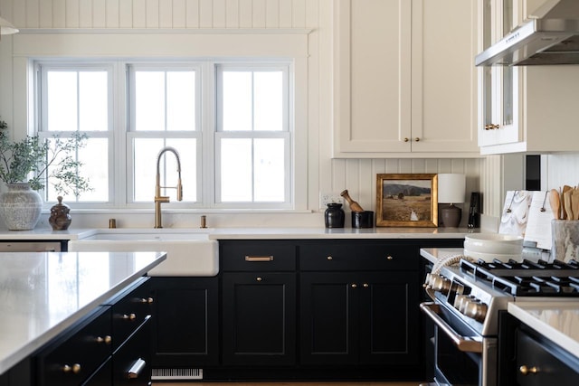 kitchen with a sink, light countertops, under cabinet range hood, stainless steel gas stove, and dark cabinets