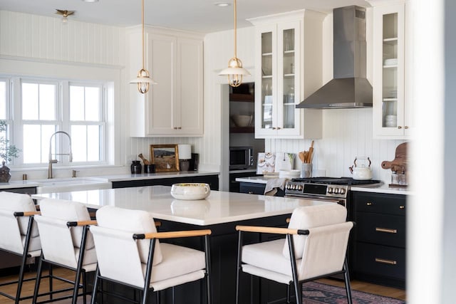 kitchen with light countertops, white cabinetry, wall chimney exhaust hood, a kitchen bar, and a center island